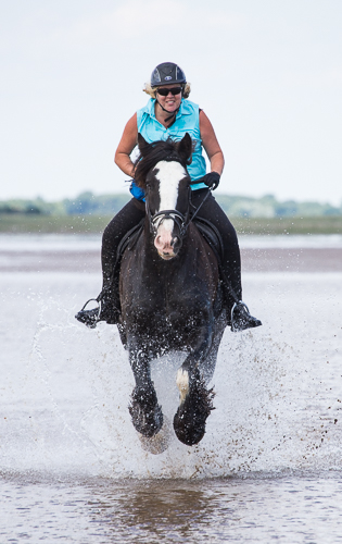 Horse and rider galloping through water on beach all four feet off the ground
